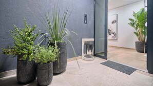 Een moderne receptiebalie met een gestructureerde wand, plantenpotten, een glazen deur en een minimalistisch interieur.