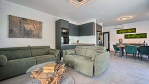 Ein modernes Wohnzimmer mit einem grünen Sofa, einem Glastisch und einem Essbereich mit einem grünen Sessel und einem Tisch.