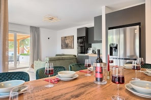 A modern living room with a dining area, a sofa, a coffee table, and a kitchen in the background.