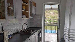 Cocina moderna con armarios blancos, encimera negra y vista a una piscina a través de una puerta abierta.