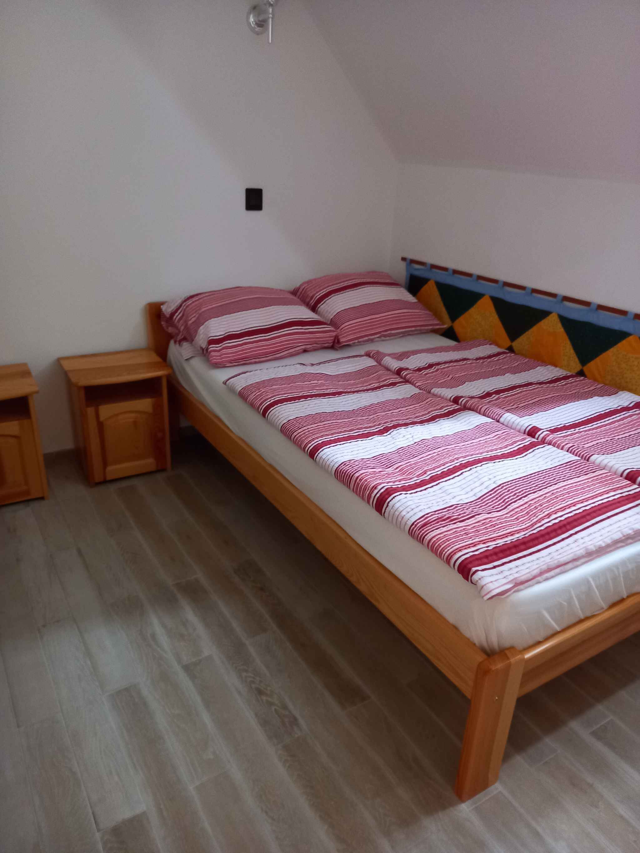 Una camera con un letto singolo, una struttura in legno, una coperta a righe, due comodini in legno e una testiera colorata.