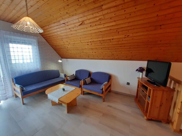 A cozy living room with a wooden ceiling, a sofa set, a coffee table, and a TV on a wooden stand. - Holiday home with view and pool (Balatongyörök)