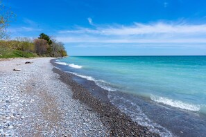 A pebbled beach with clear turquoise water and a clear sky.