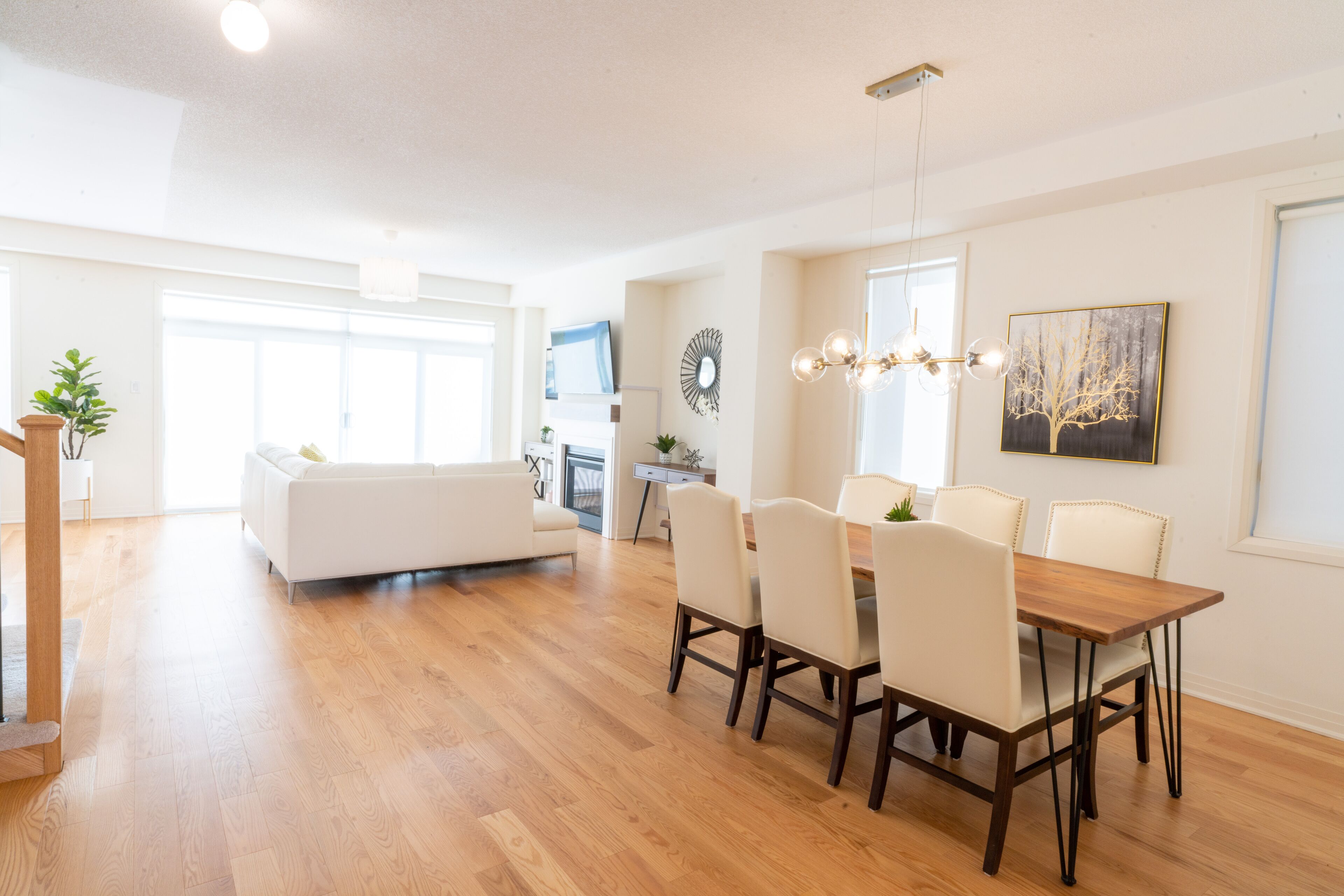 A spacious living area with a wooden floor, a white sofa, a dining table with chairs, and a chandelier.