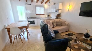 Un espacio habitable compacto con kitchenette, comedor y zona de estar con sofá y mesa de centro.