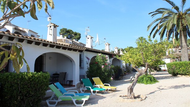 Un patio con mobiliario exterior, una palmera y un edificio con arcos y techo de tejas.