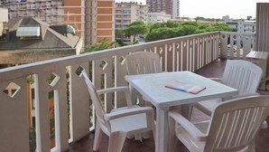 A balcony with a table and chairs, a view of buildings, and a tiled floor. - Holiday apartment with balcony and air conditioning (Lignano Sabbiadoro)