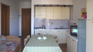 A compact kitchen with a dining table, chairs, a stove, and a television. - Holiday apartment with balcony and air conditioning (Lignano Sabbiadoro)
