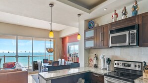 A modern kitchen with a large island, stainless steel appliances, and a view of the ocean.