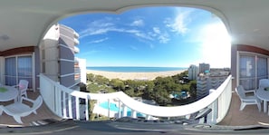 Un balcón con vista a una playa, una piscina y edificios circundantes.