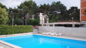 Una piscina con lettini, una recinzione e un edificio con segnaletica sullo sfondo.