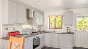 A modern kitchen with white cabinetry, a stainless steel range hood, a built-in oven, and a window with a view of greenery. - Brook Cottage - village cottage close to pubs and walks (Coniston)