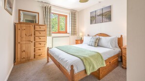 A bedroom with a wooden bed, a nightstand, a dresser, a window with curtains, and a painting on the wall. - Brook Cottage - village cottage close to pubs and walks (Coniston)