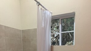 A bathroom with a shower, a toilet, and a window with a view of foliage. - The Cottage (Kingston)