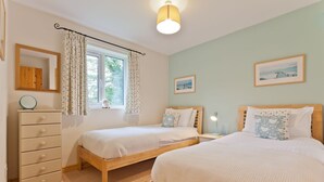 A bedroom with two single beds, a dresser, a window with curtains, and a ceiling light. - Yewdale Cottage, village home with mountain views (Coniston)