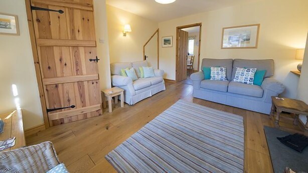 A cozy living room with a wooden door, two sofas with patterned cushions, a striped rug, and a small table. - Yewdale Cottage, village home with mountain views (Coniston)