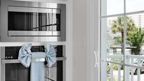 Une cuisine équipée de deux fours en acier inoxydable, d’un four à micro-ondes et d’une fenêtre donnant sur un quartier résidentiel.