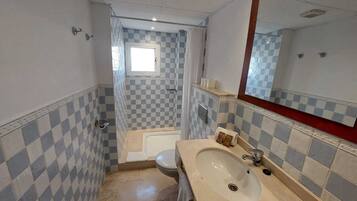 A bathroom with checkered tile walls, a bathtub, a toilet, and a sink with a mirror.