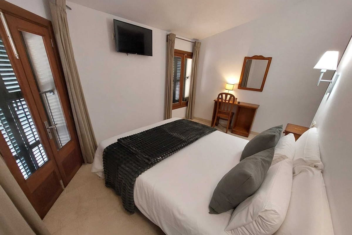 Una habitación de hotel con cama, escritorio, silla, televisor y espejo.
