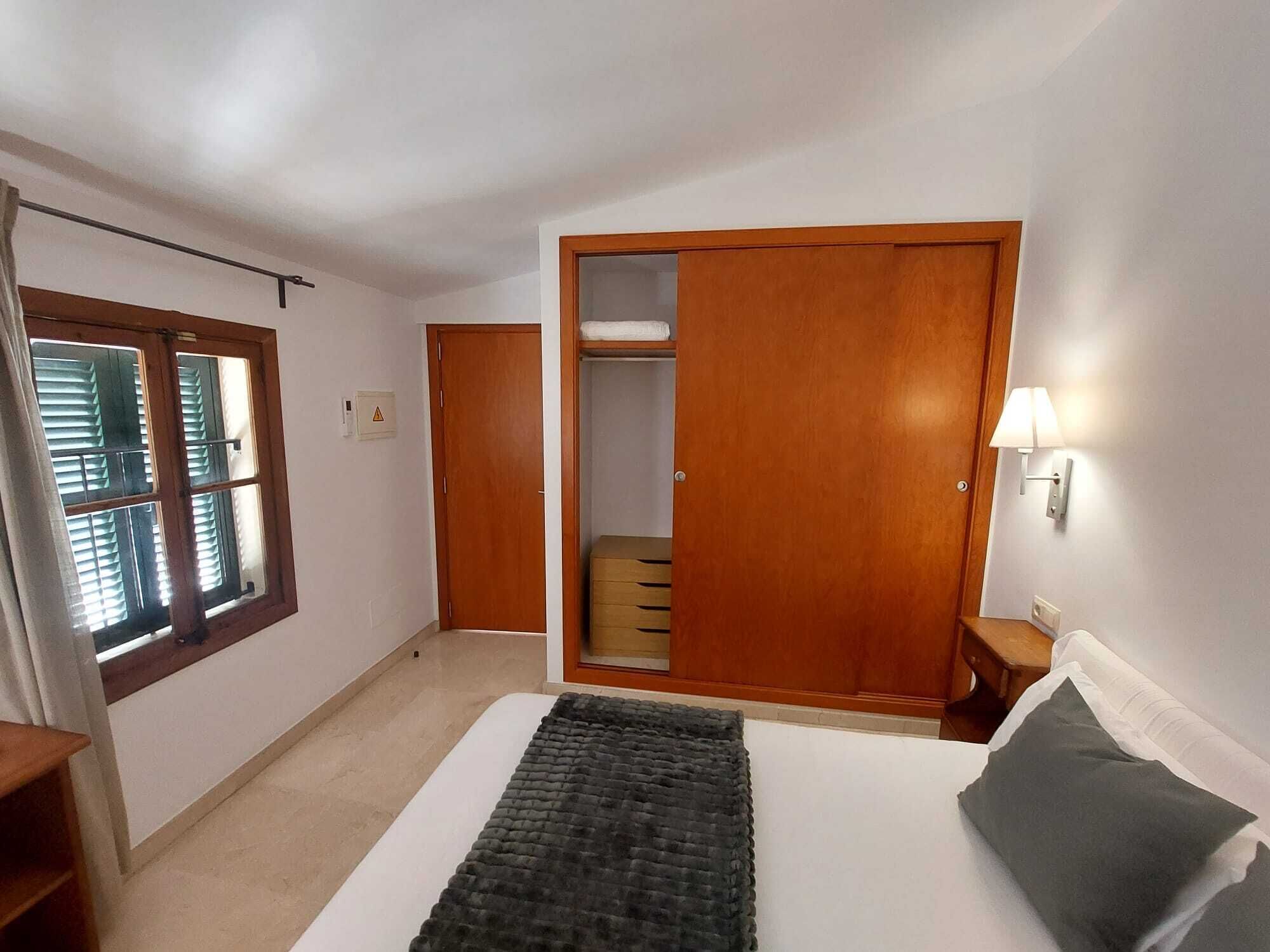 Un dormitorio con cama, armario, mesita de noche y ventana con persianas.