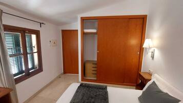 Un dormitorio con cama, armario, mesita de noche y ventana con persianas.