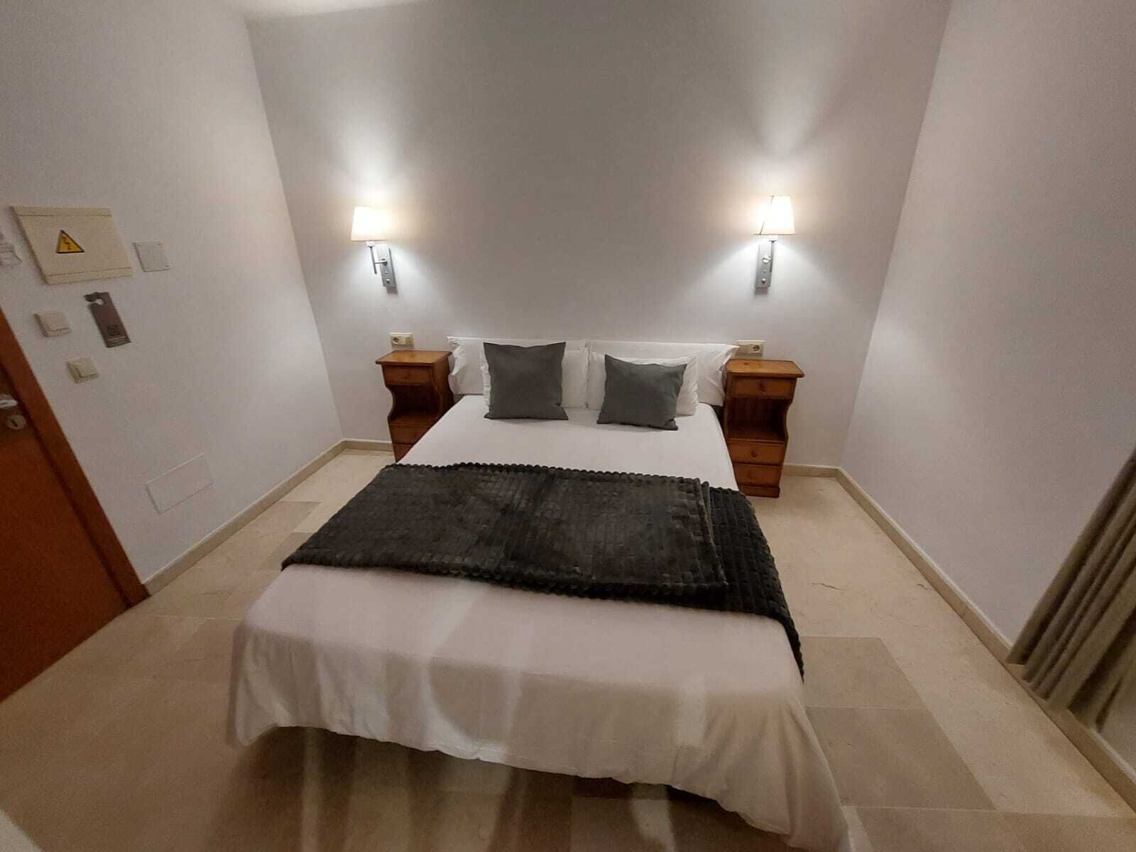 Ein ordentlich eingerichtetes Schlafzimmer mit einem Bett, zwei Nachttischen und Wandlampen.
