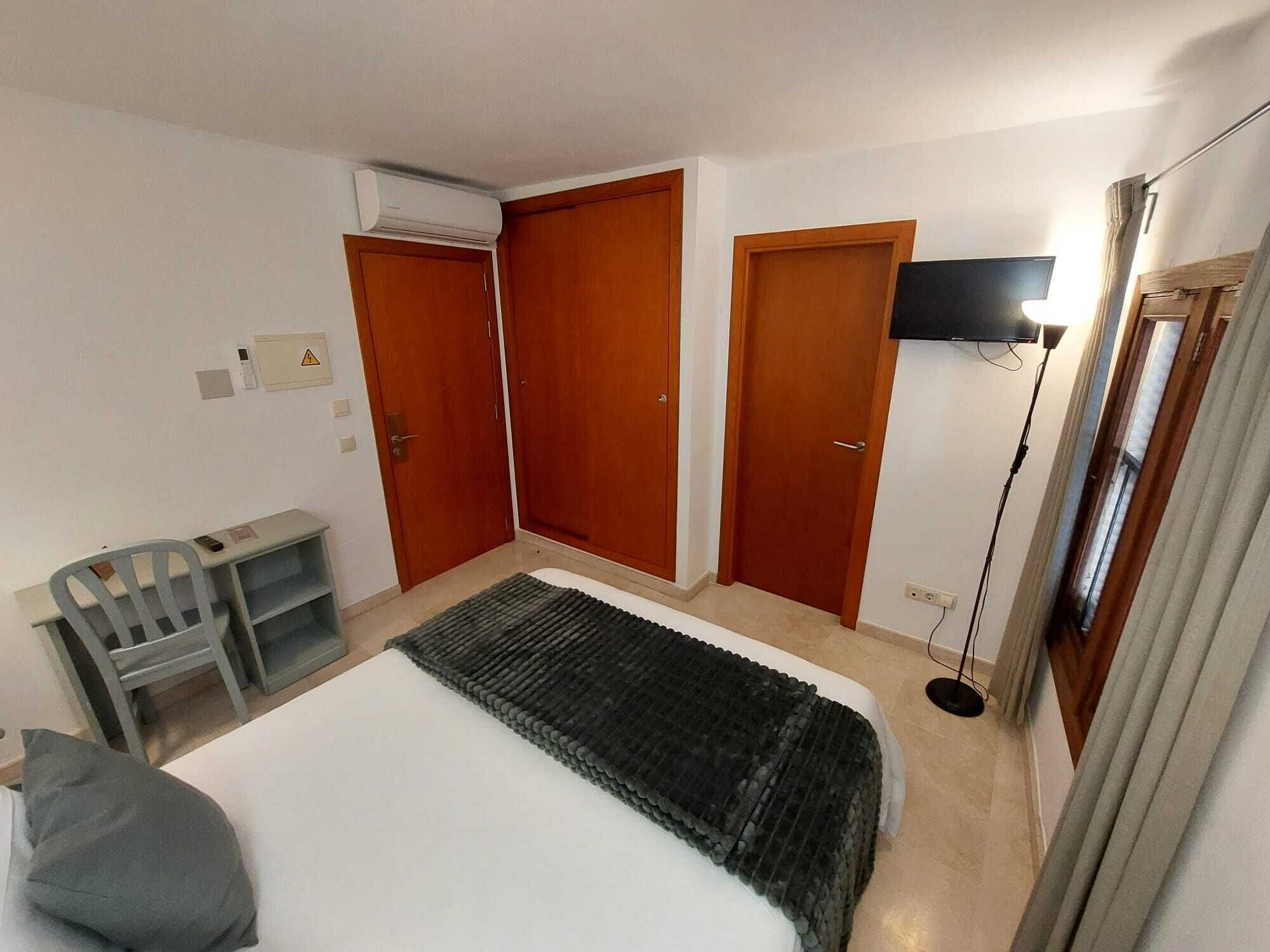 Una habitación de hotel con una cama, un escritorio, una silla, un televisor y dos armarios.