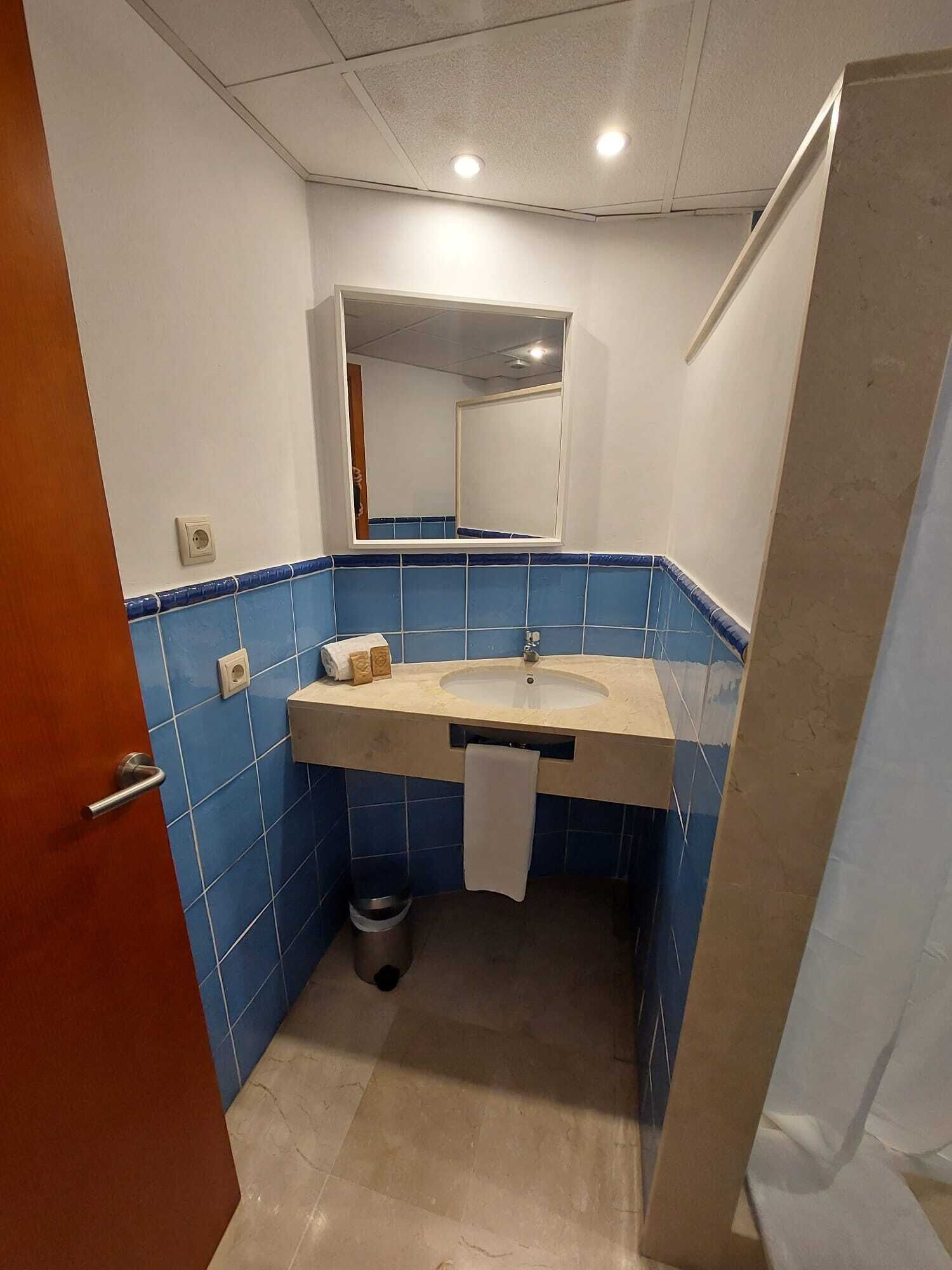 Un baño pequeño con lavamanos, espejo y paredes con azulejos azules.