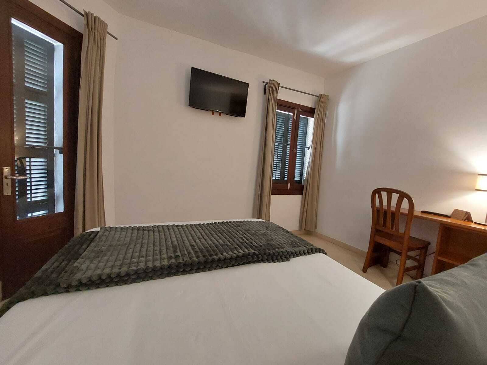 Une chambre d’hôtel équipée d’un lit, d’un bureau, d’une chaise, d’une télévision et d’une fenêtre avec des rideaux.