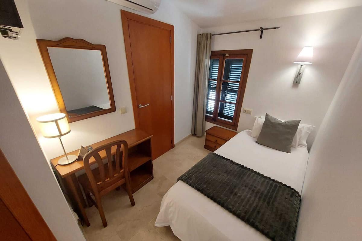 Un dormitorio con cama, escritorio, silla, armario y ventana con persianas.