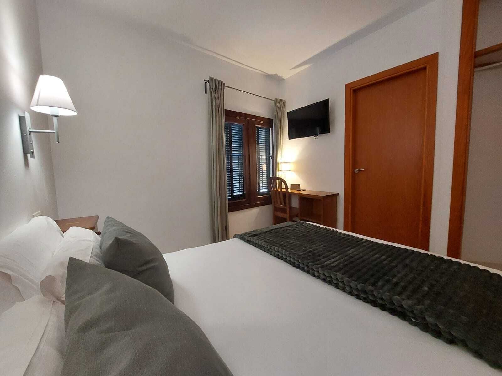 Una habitación de hotel con cama, escritorio, silla, televisor y puerta.