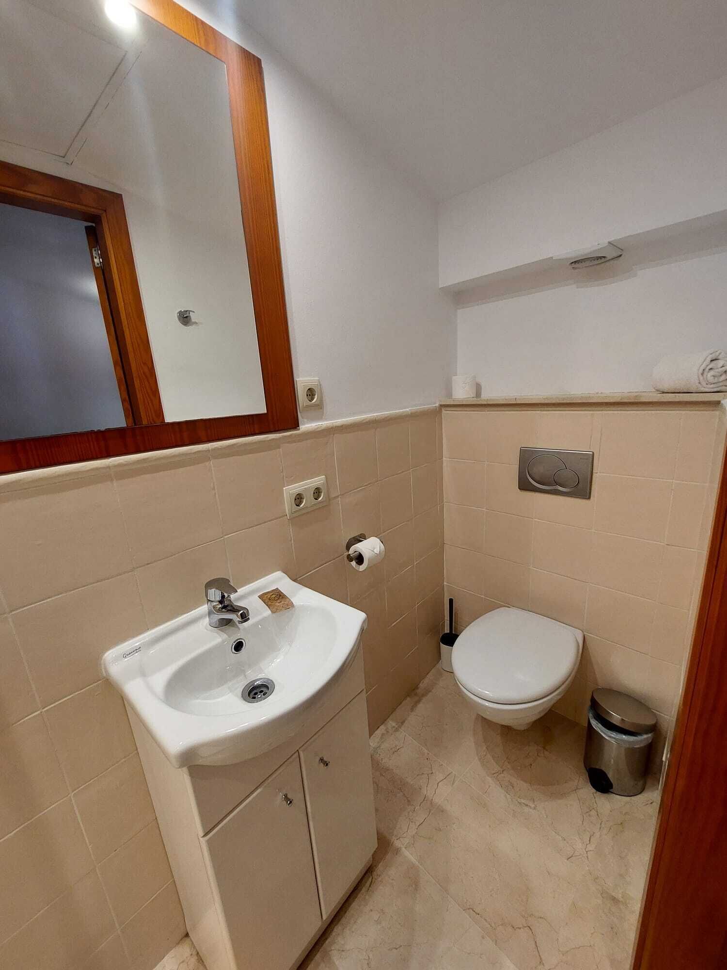 A small, clean bathroom with a white sink, a toilet, and a trash bin.
