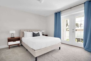 Une chambre à coucher avec un lit, une table de chevet et une vue sur l’extérieur, visible à travers une porte.