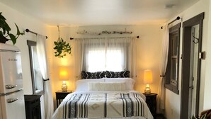 Une chambre à coucher avec un lit, des lampes de chevet, une commode, un miroir, une fenêtre avec des rideaux et une plante en pot.