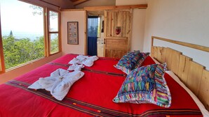 A bedroom with a large bed, wooden headboard, and a view of the outdoors.