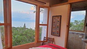A room with a bed, a window with a view of the sea, and a wall-mounted picture.