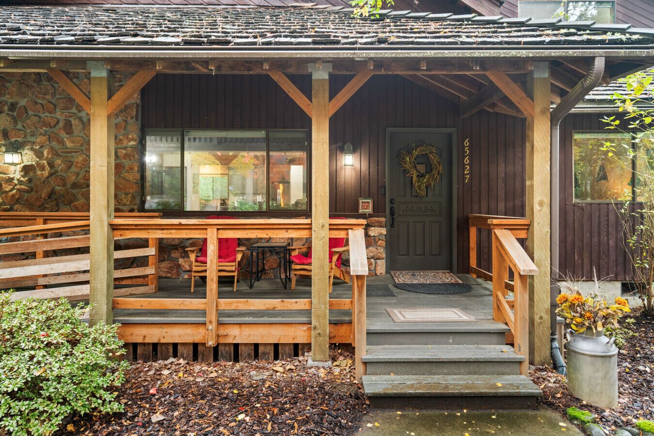 A wooden porch with a stone wall, a door with a wreath, and a small table with chairs.