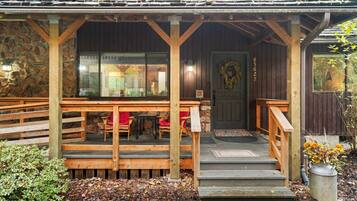 A wooden porch with a stone wall, a door with a wreath, and a small table with chairs.