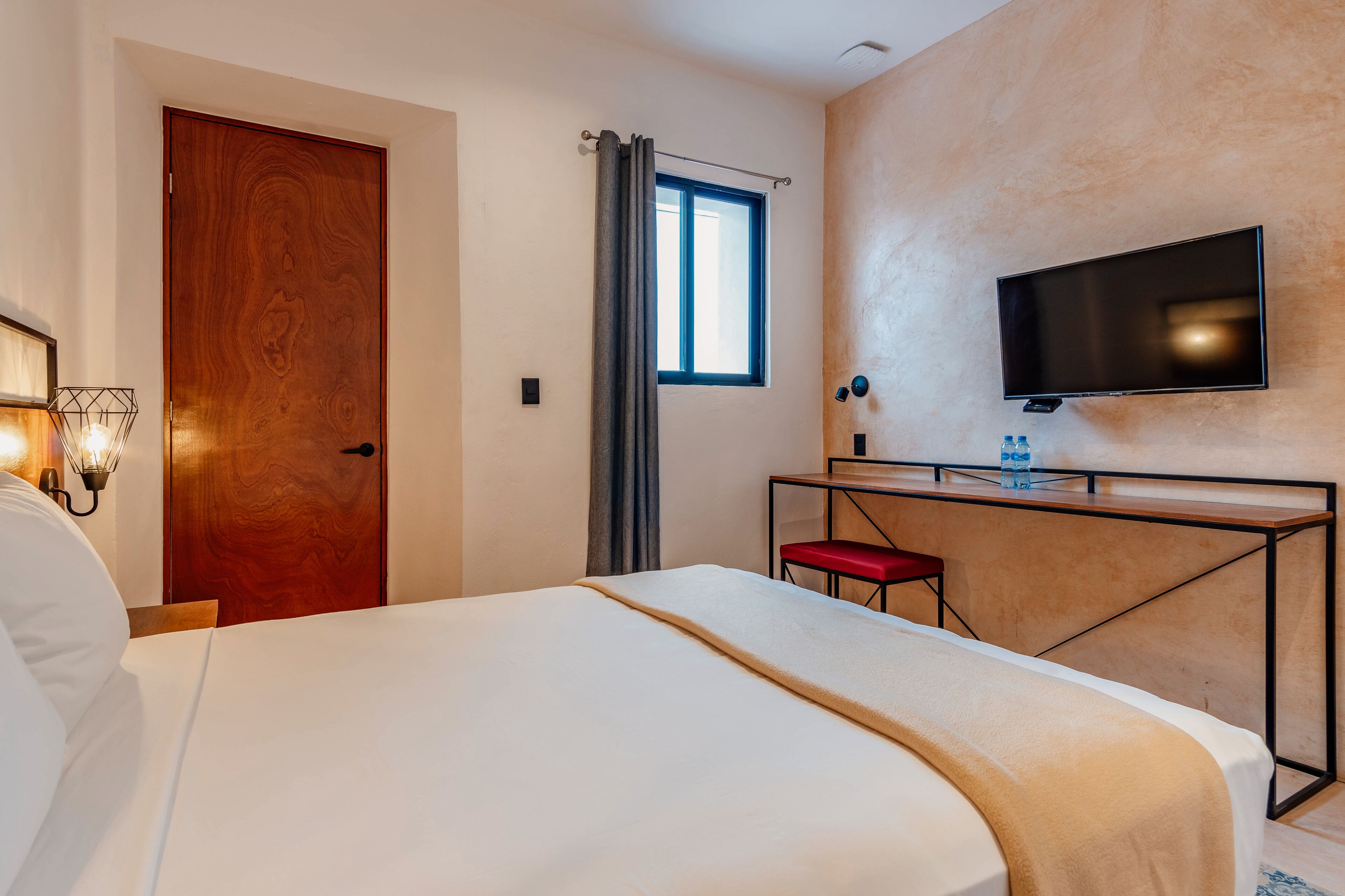 Una habitación de hotel con cama, escritorio, televisión y ventana.