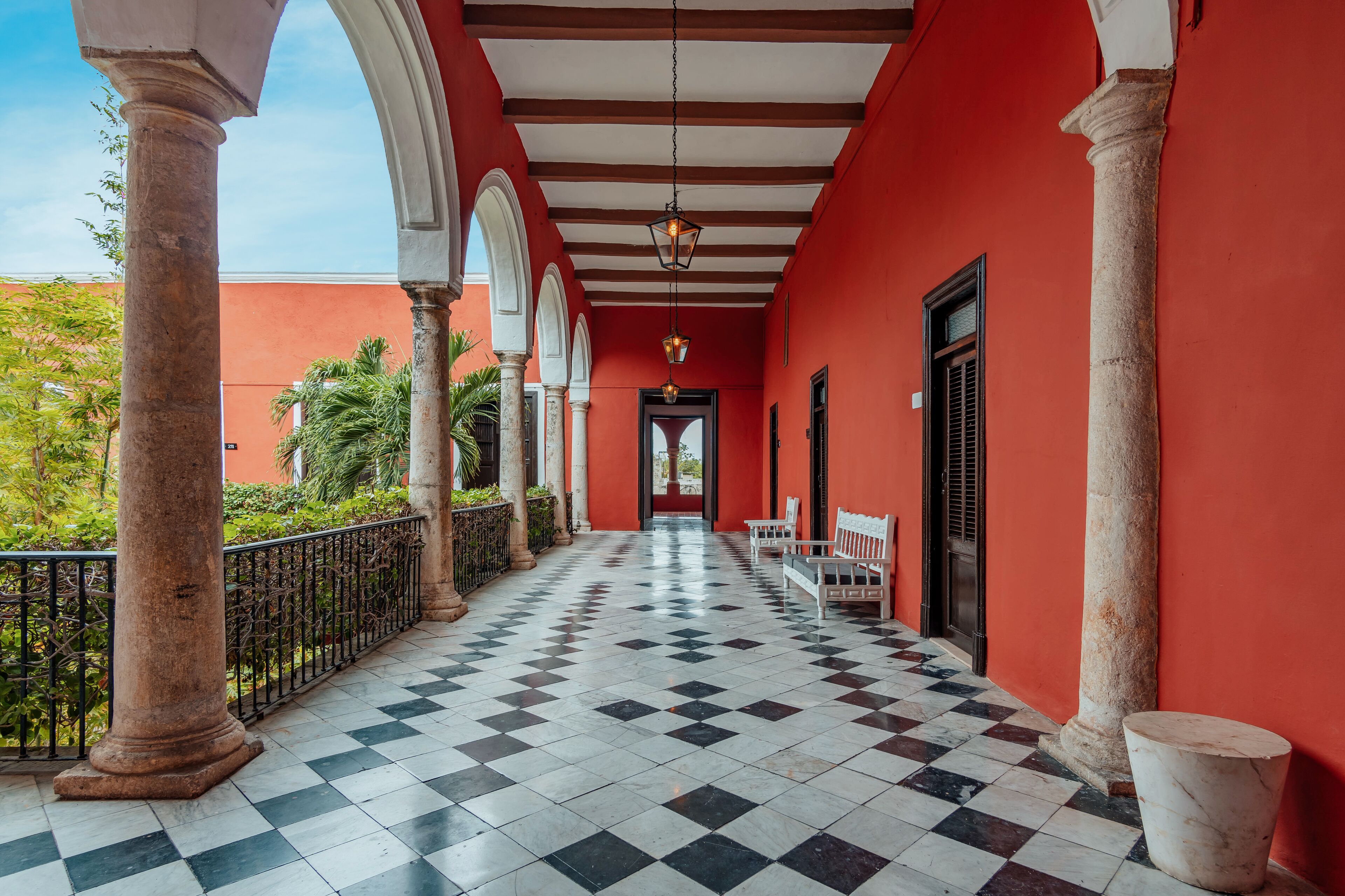 A corridor with checkered flooring, columns, and a bench.