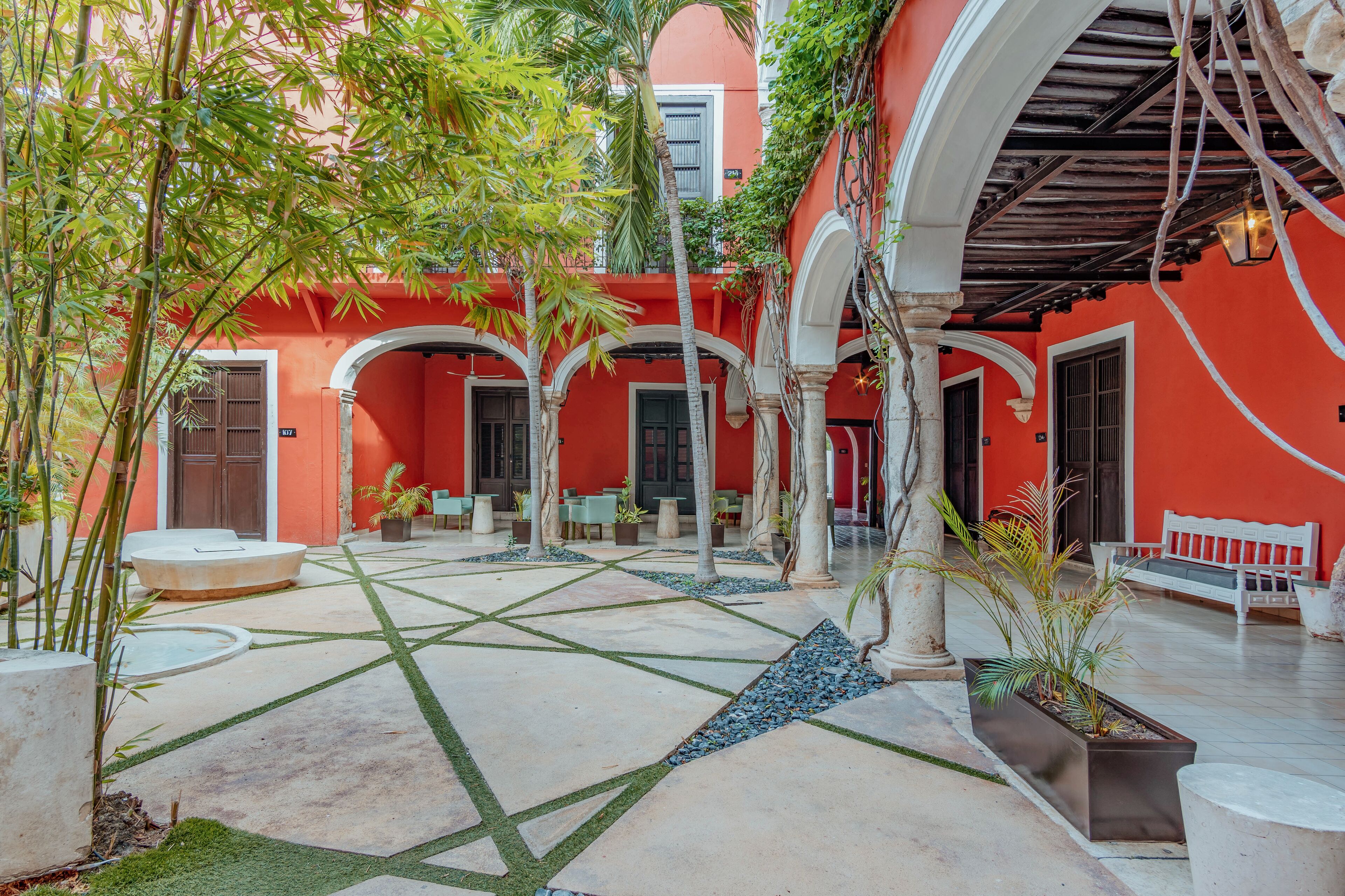 A courtyard with red walls, white columns, and a tiled floor. There are potted plants and a bench.