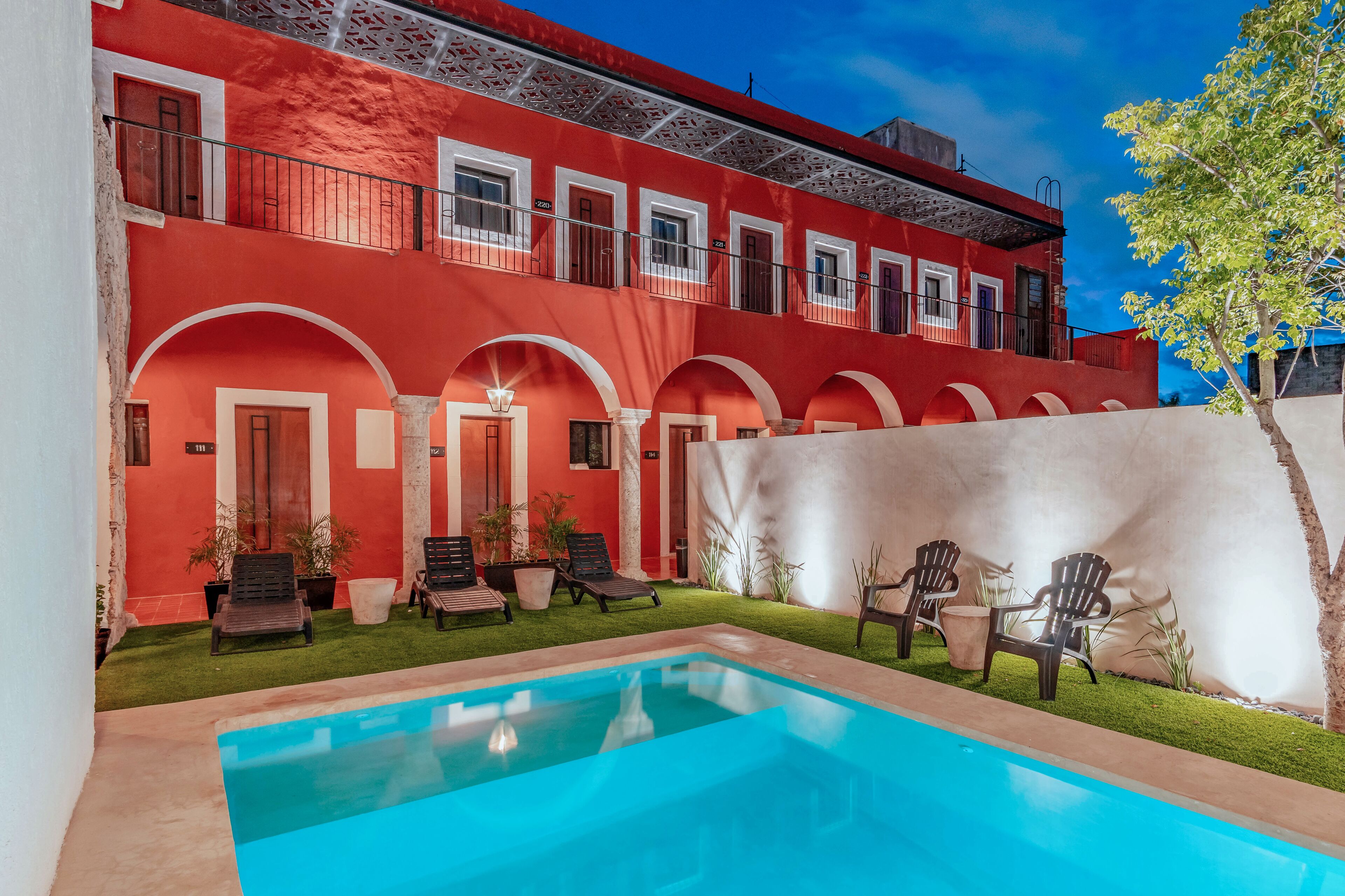 A red building with a swimming pool, outdoor seating, and a tree.