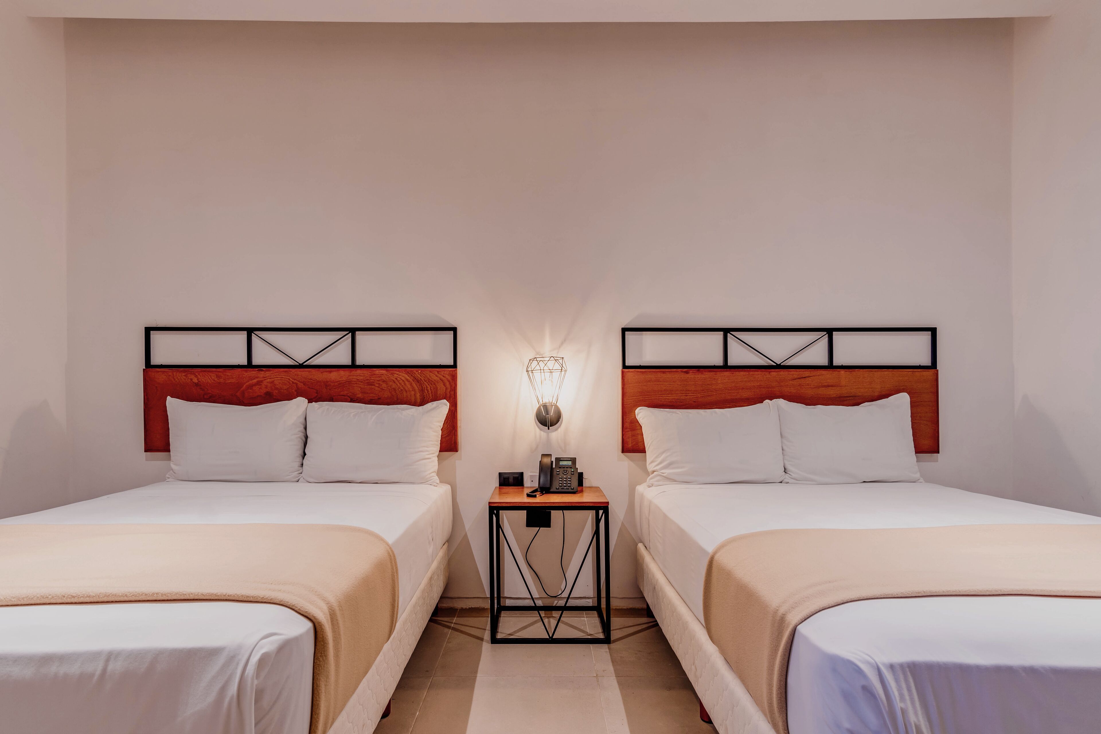Ein Hotelzimmer mit zwei Einzelbetten, einem kleinen Nachttisch mit Lampe und einem Holzkopfteil.