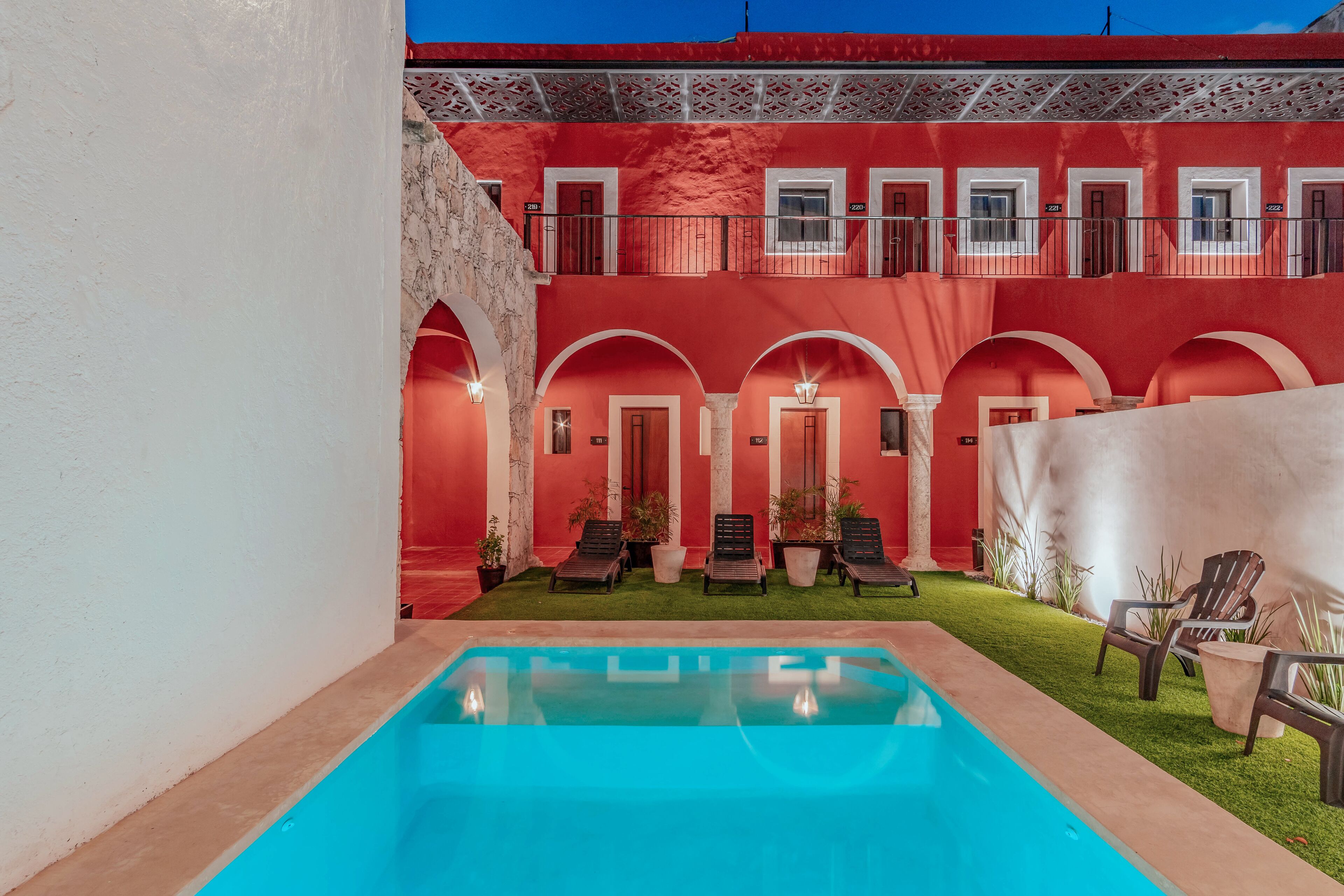 A red building with a pool and lounge chairs.