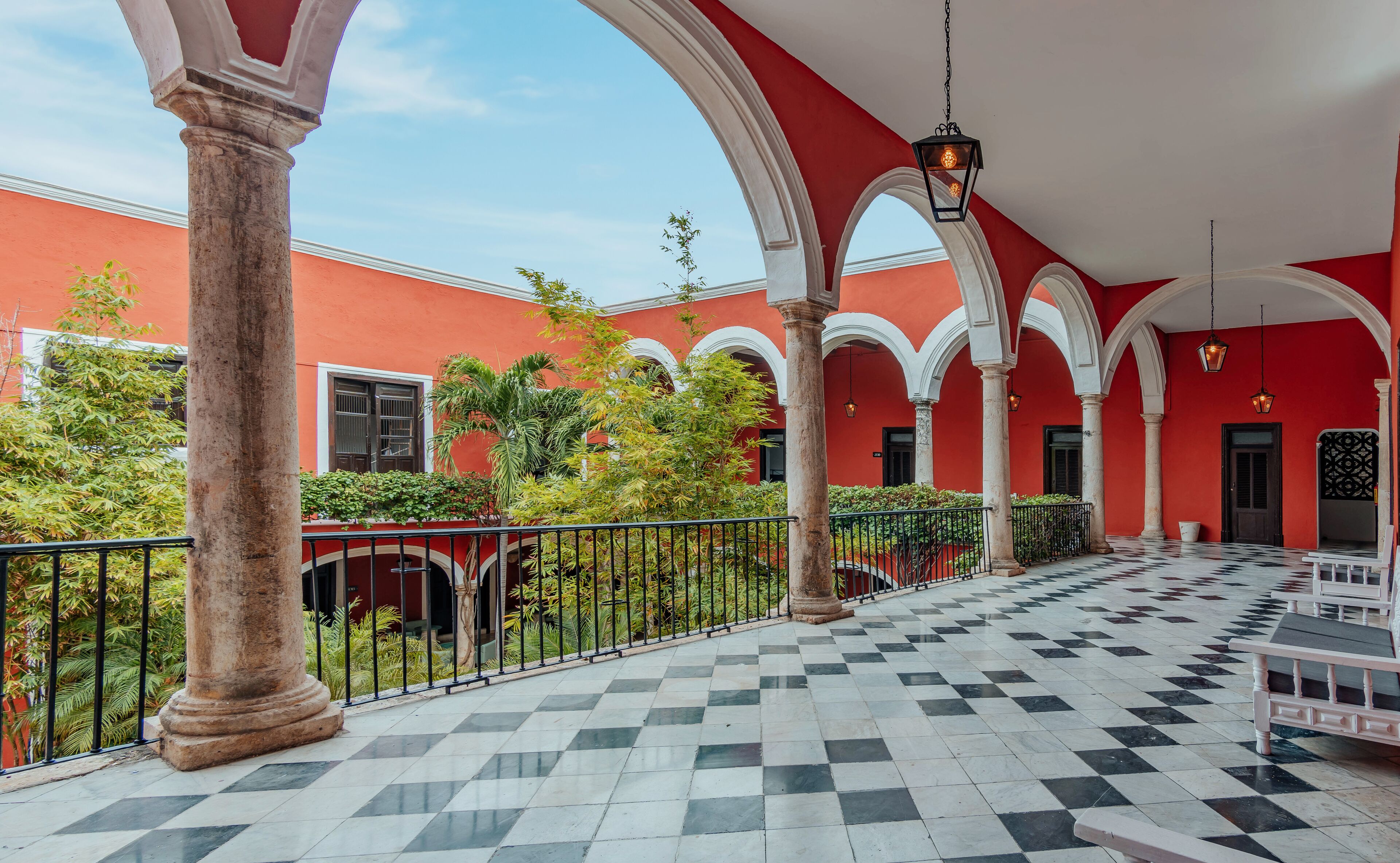 Un patio con piso a cuadros, paredes rojas y arcos blancos.