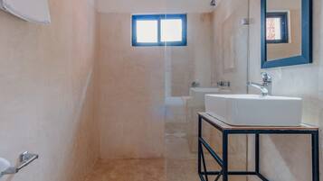 Un baño moderno con cabina de ducha de vidrio, un lavabo blanco y un ventanal.