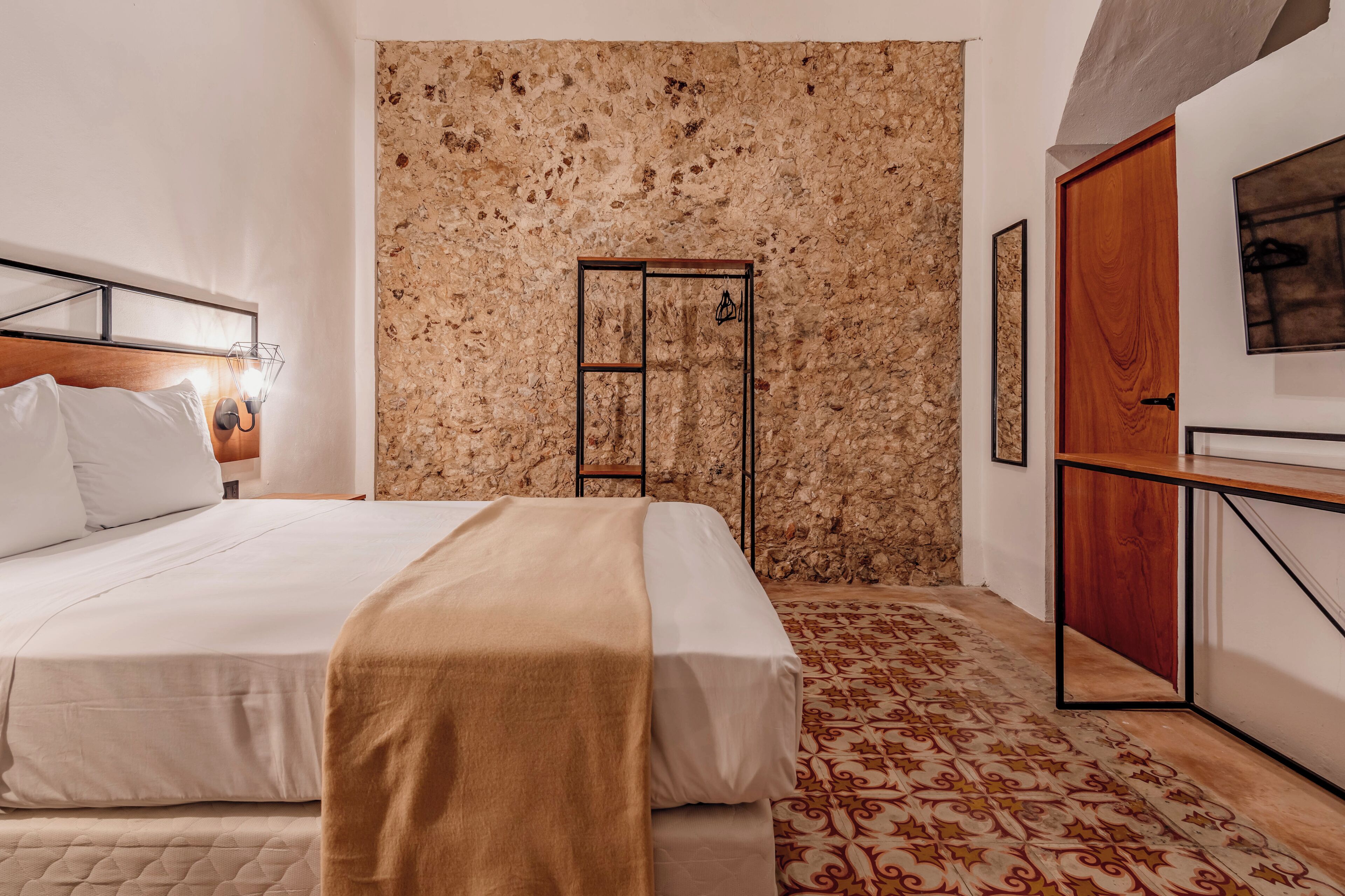 Un dormitorio con una cama, una puerta de madera, un muro de piedra y una alfombra estampada.