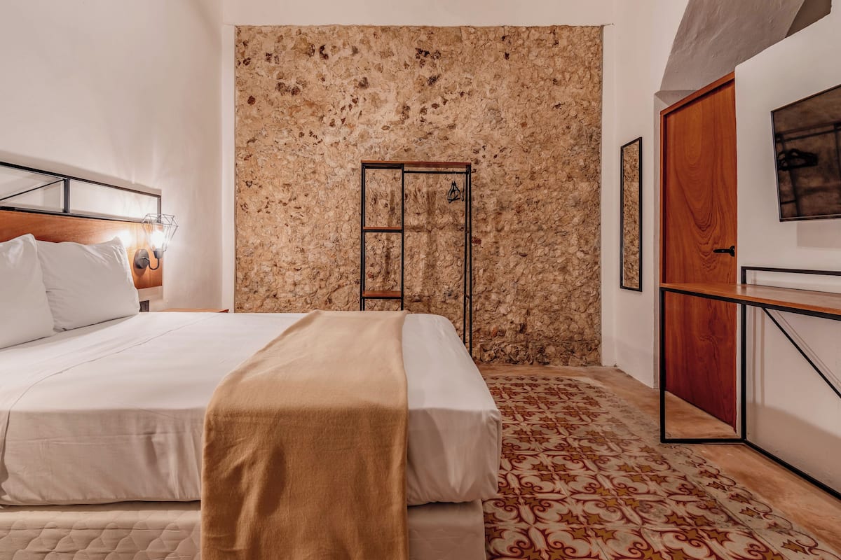 Un dormitorio con una cama, una puerta de madera, un muro de piedra y una alfombra estampada.