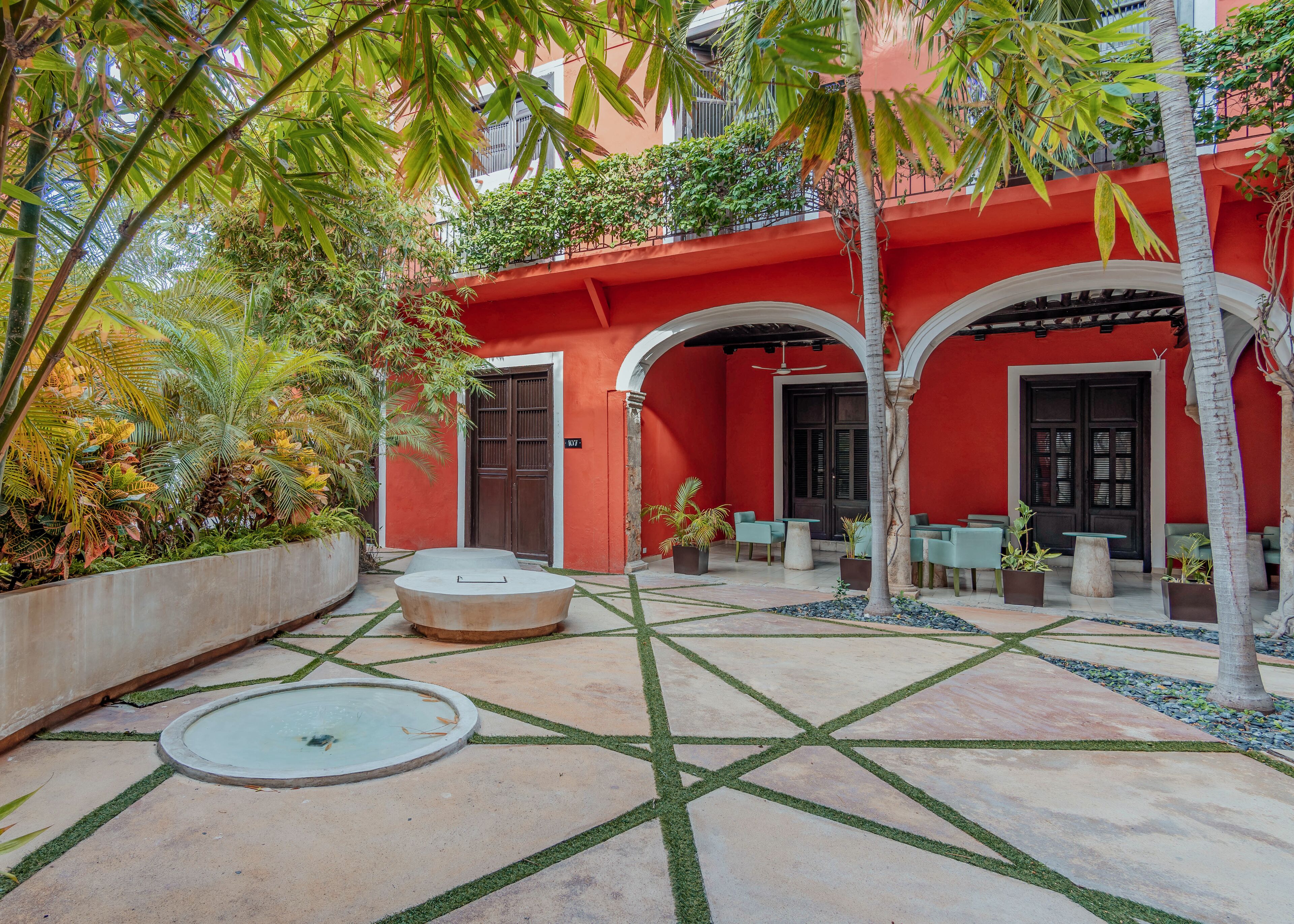 Une cour avec un bâtiment rouge, des sièges en plein air et une petite fontaine.
