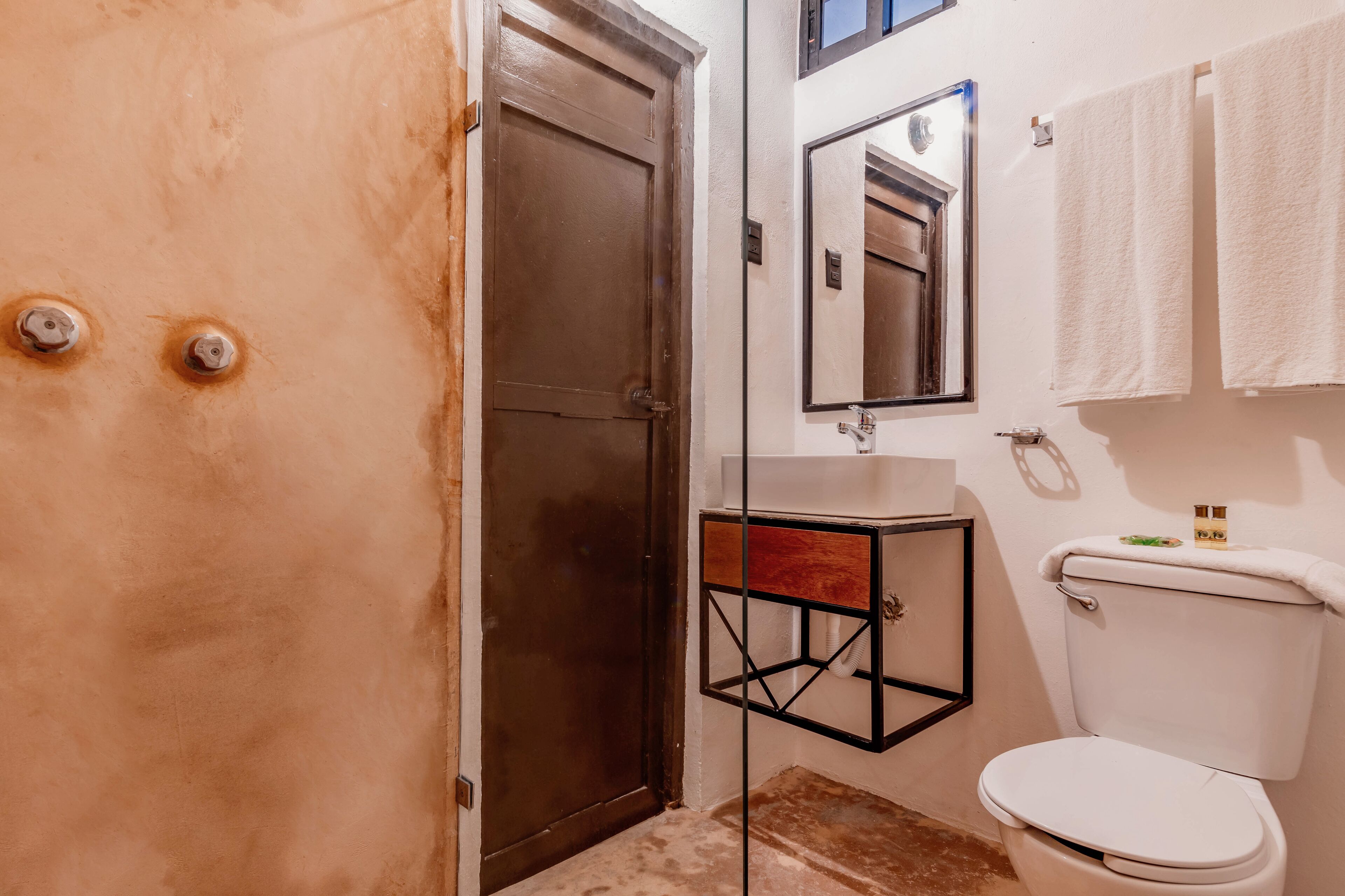 Un baño con inodoro, lavamanos, espejo y toallero.